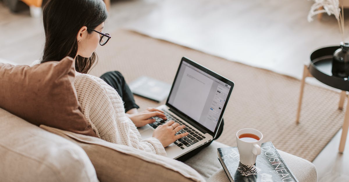 Bringing coins back home from abroad; Is that unethical to do? - From above back view of full length female freelancer with crossed legs sitting on cozy sofa with cup of tea on book while typing text on laptop