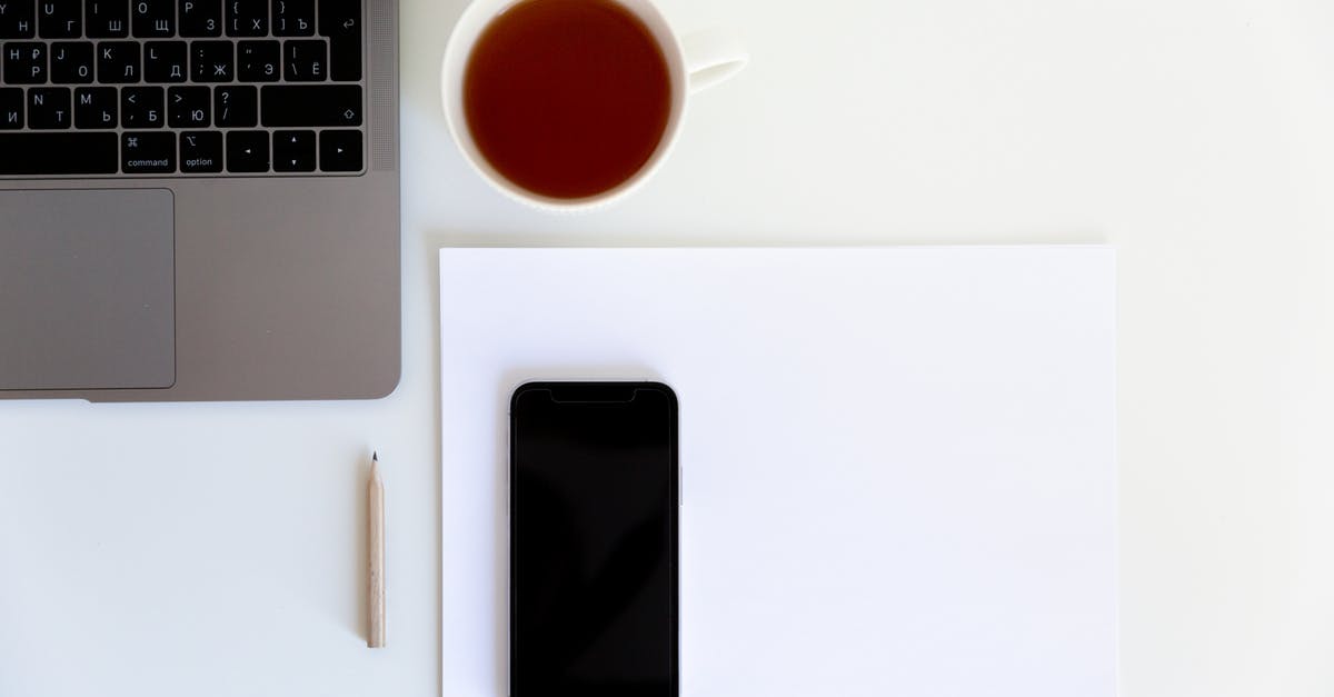 Bringing laptop with US keyboard layout back into the UK - Workplace with smartphone placed on white paper with cup of tea aside near laptop and pencil