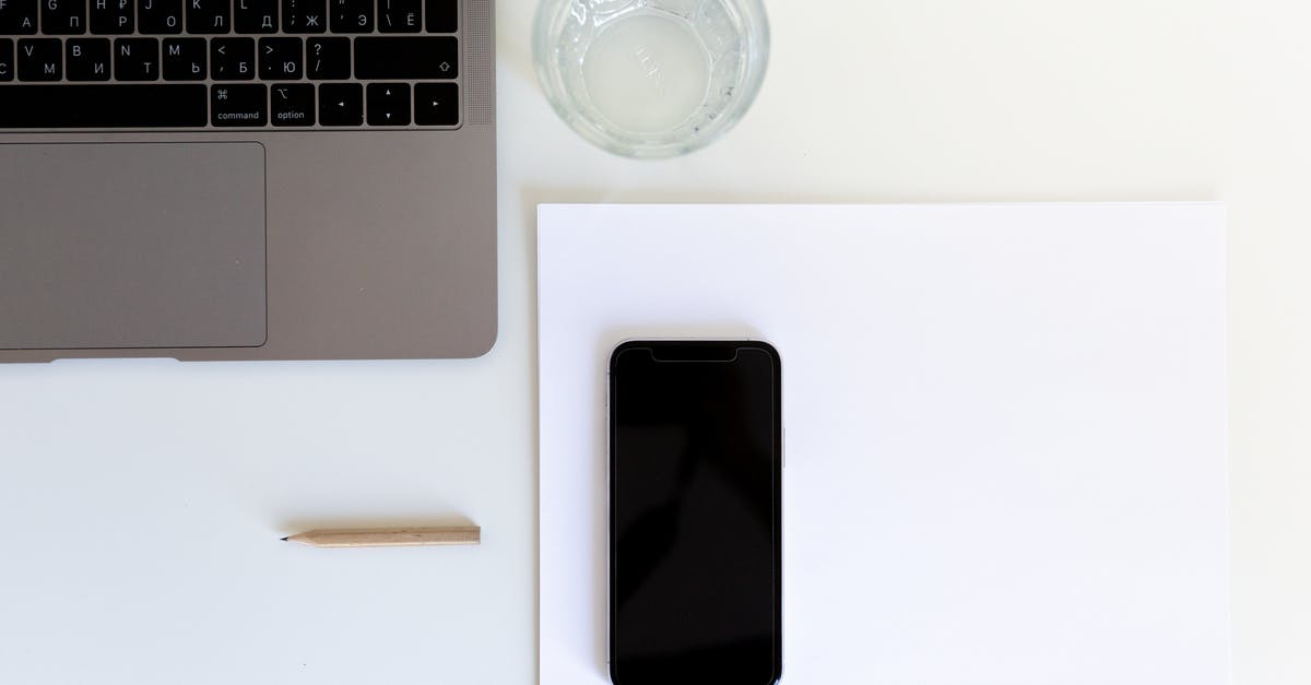 Bringing laptop with US keyboard layout back into the UK - From above of smartphone placed on white paper with laptop and glass of water preparing for working day in modern workplace