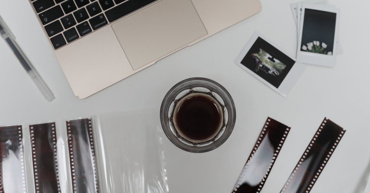 Bringing laptop with US keyboard layout back into the UK - Top view of coffee cup with vintage instant photos and negative film strips placed on table with opened laptop