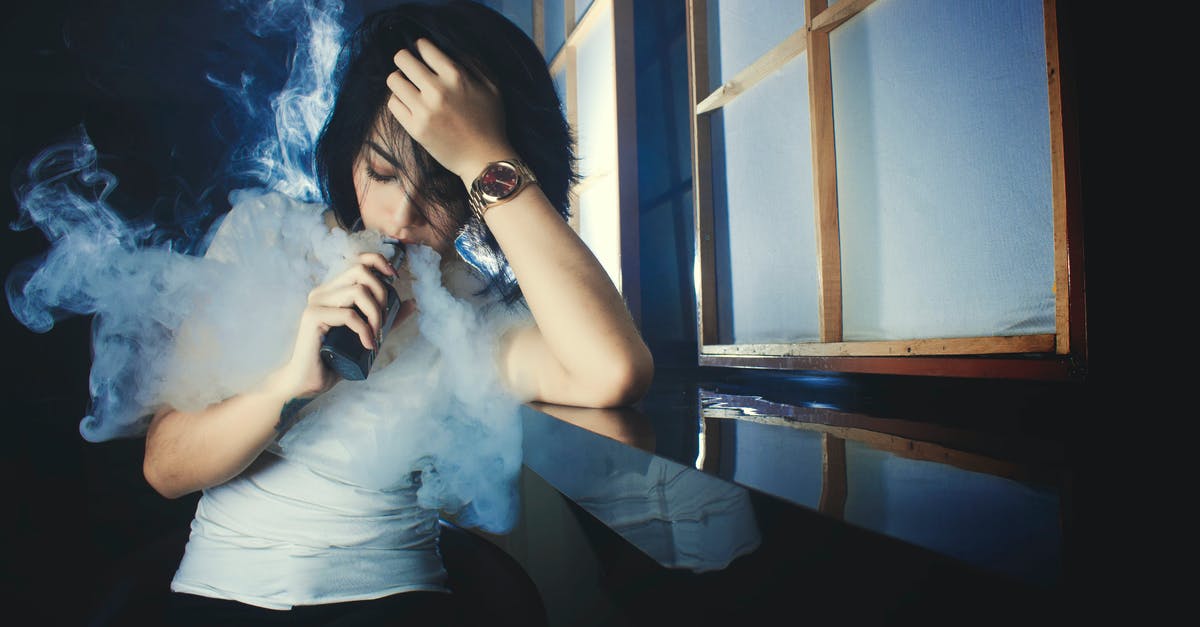 Bringing nicotine e-liquids to Australia - Cool casual brunette in white t shirt smoking electronic cigarette while leaning on hand in dark studio