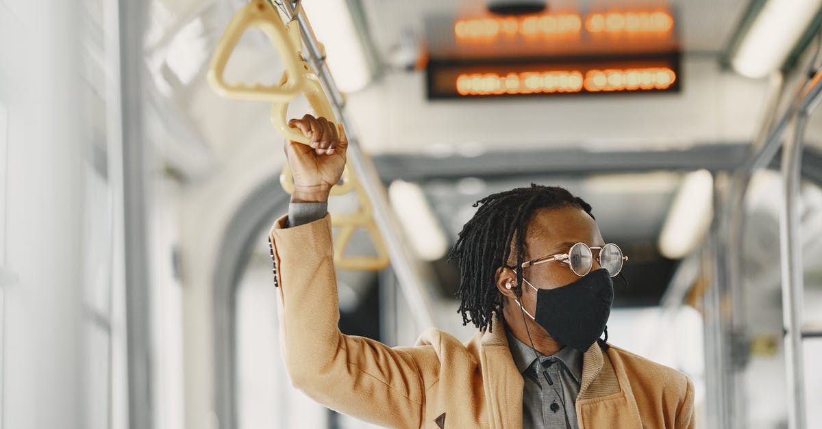 Bus schedule Thessaloniki - Litochoro - Man in Brown Coat Wearing Facemask and Eyeglasses Holding on Bus Handle 