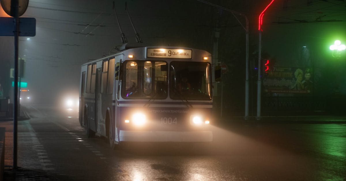 Bus service between small towns in Spain - Old trolleybus driving along wet asphalt road in small city at foggy night