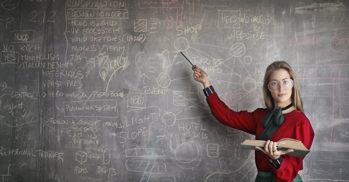 Business class fully booked! - Serious female teacher wearing old fashioned dress and eyeglasses standing with book while pointing at chalkboard with schemes and looking at camera