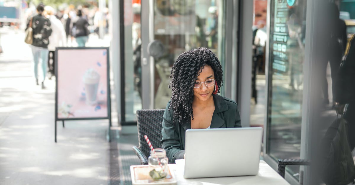 Business name and what visa to use for Canada? [closed] - High angle of pensive African American female freelancer in glasses and casual clothes focusing on screen and interacting with netbook while sitting at table with glass of yummy drink on cafe terrace in sunny day