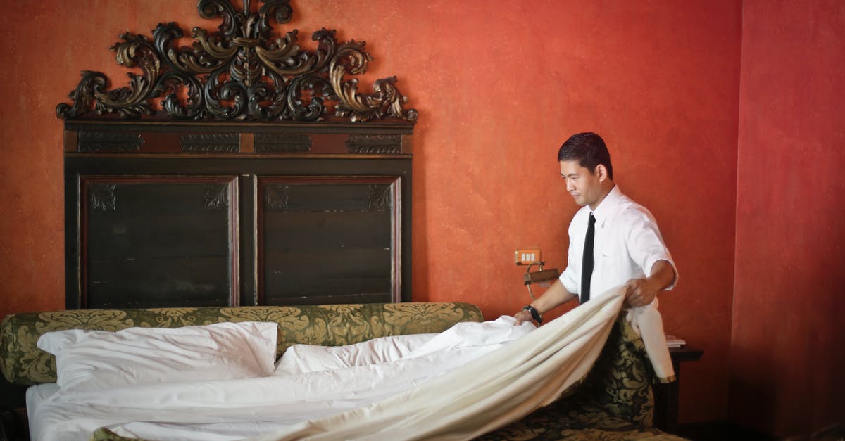 Business travel basis accommodation? - Side view of young ethnic male making bed while cleaning stylish hotel room with vintage furniture and red walls