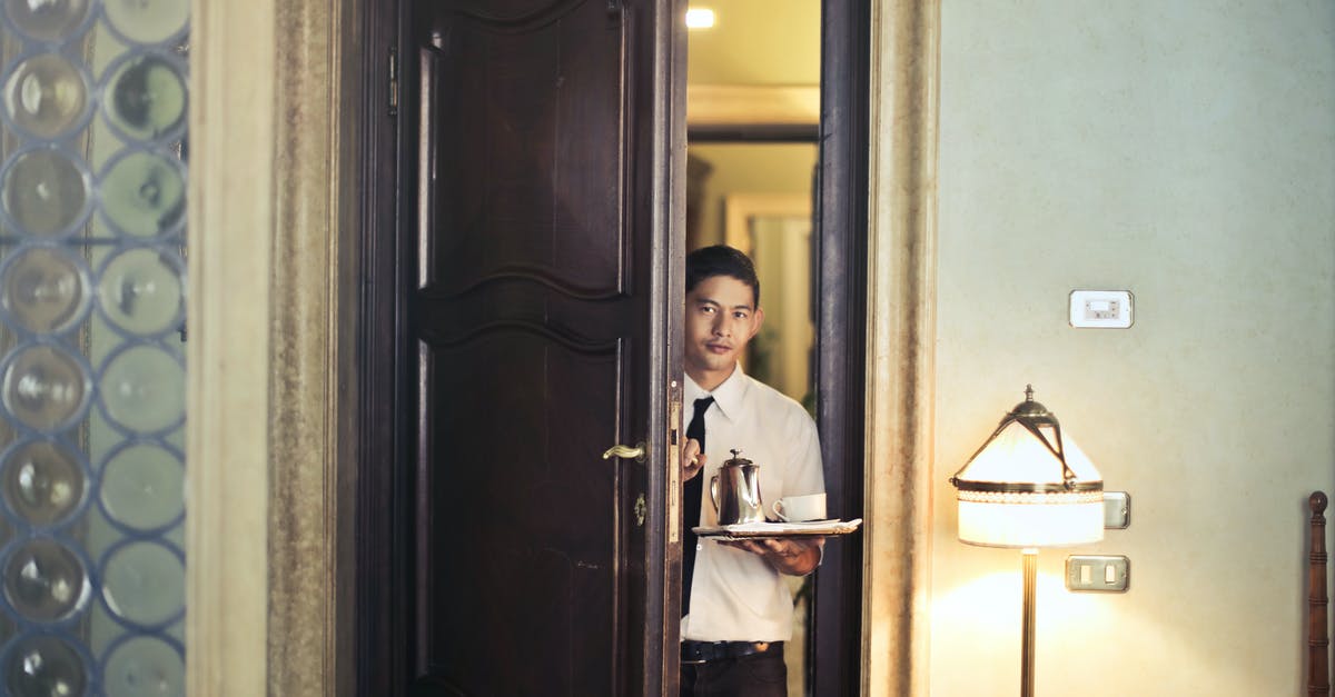 Business travel basis accommodation? - Young ethnic male room service waiter carrying tray with coffee pot while entering hotel room with stylish vintage interior