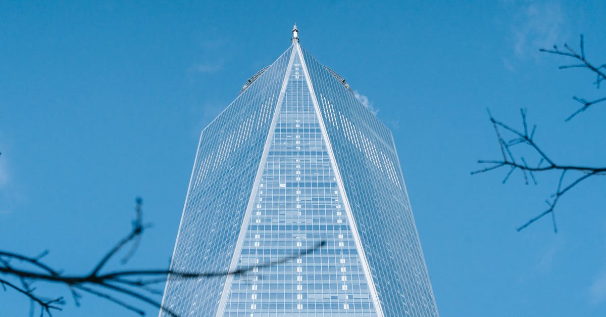 Business Travel to US for 5 months - Low angle of geometric facade of modern creative skyscraper with glass walls against cloudless blue sky in New York City