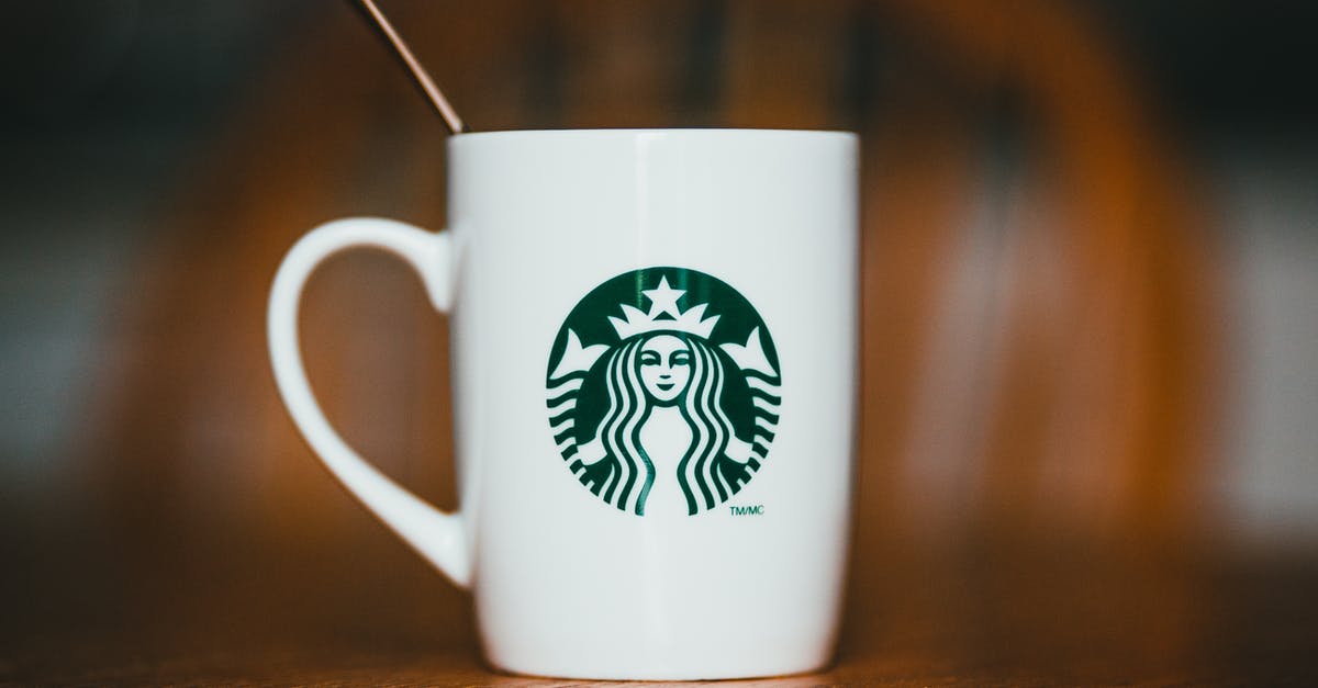 Buy and taste tea in China [closed] - Closeup of white ceramic mug with logotype of brand with hot drink and teaspoon placed on wooden table