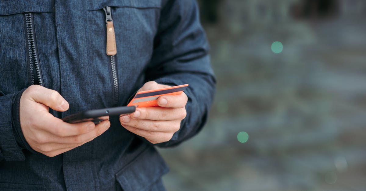 Buy credits for prepaid mobile in another country - Man holding credit card and browsing smartphone on street