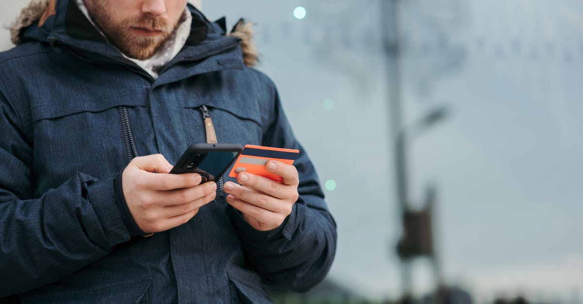 Buy credits for prepaid mobile in another country - Crop concentrated man in warm clothes entering credentials of credit card on mobile phone while standing in street in daytime