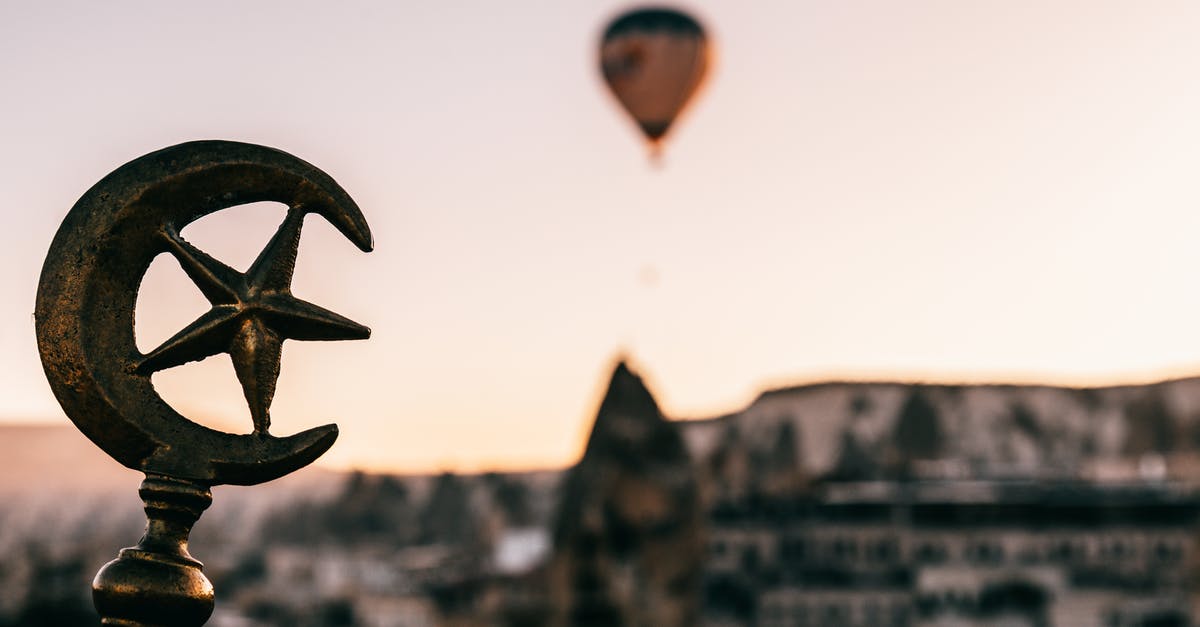 Buying a flight ticket to the UK for a foreign national - Soft focus of Turkey symbols on top of building against floating air balloon under Cappadocia terrain at dawn