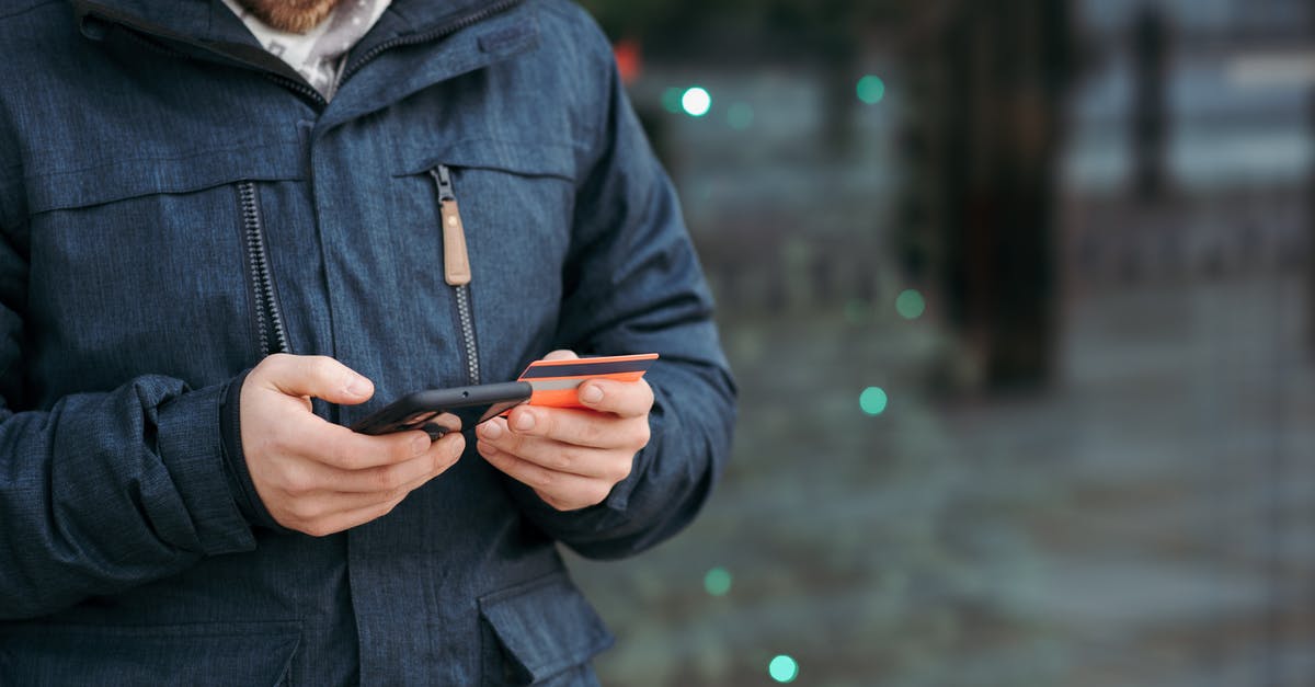 Buying a phone for using in both France and Canada - Man browsing smartphone and holding credit card on street