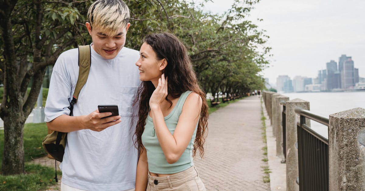 Buying a phone in the US - Positive young ethnic couple using smartphone while strolling in city park