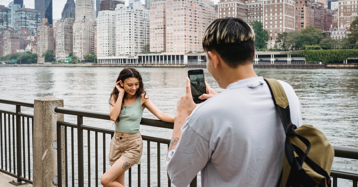 Buying a phone in the US - Young man photographing girlfriend on smartphone during date in city downtown near river