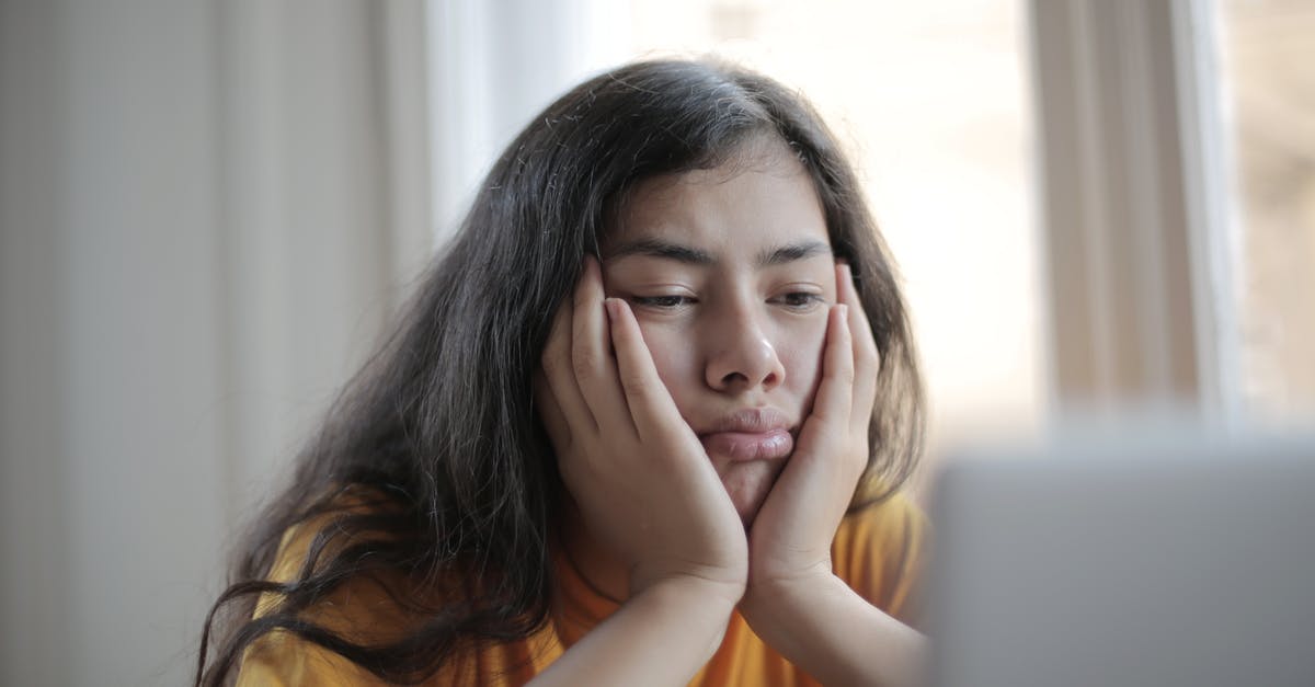 Buying domestic flights in India online - Bored ethnic female in casual clothes sitting at table with netbook and watching sad movie while resting at home during weekend