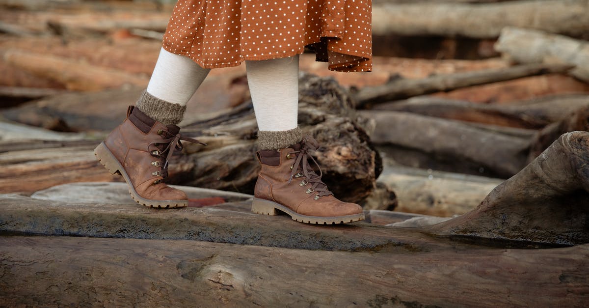 Buying extreme cold weather "mickey mouse boots" (Bunny boots) in Seoul - Unrecognizable crop woman wearing warm casual boots and skirt walking on log while spending time in countryside during weekend trip in autumn