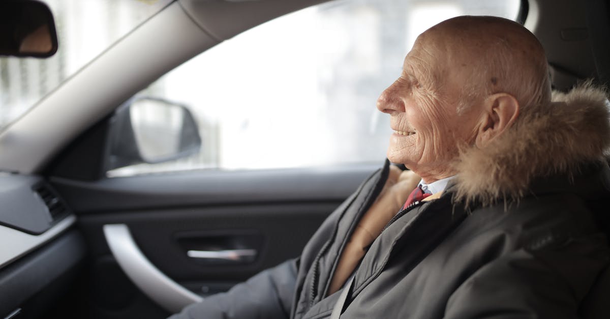 Buying Travel Insurance Whilst Abroad (UK Citizen) - Side view of content elderly male in suit and outerwear sitting in front seat of contemporary automobile and looking away