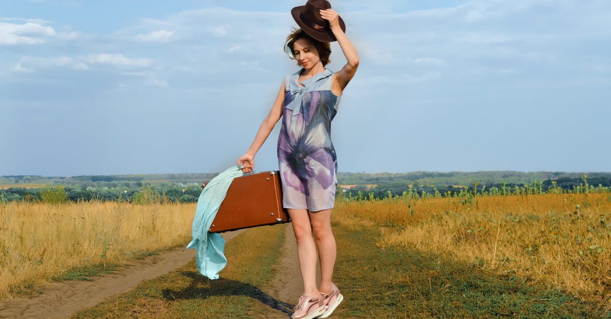 Cabin bag total linear length is 125 [closed] - Full body young female in colorful outfit with elegant hat and vintage suitcase standing on road near fields under cloudy blue sky in countryside