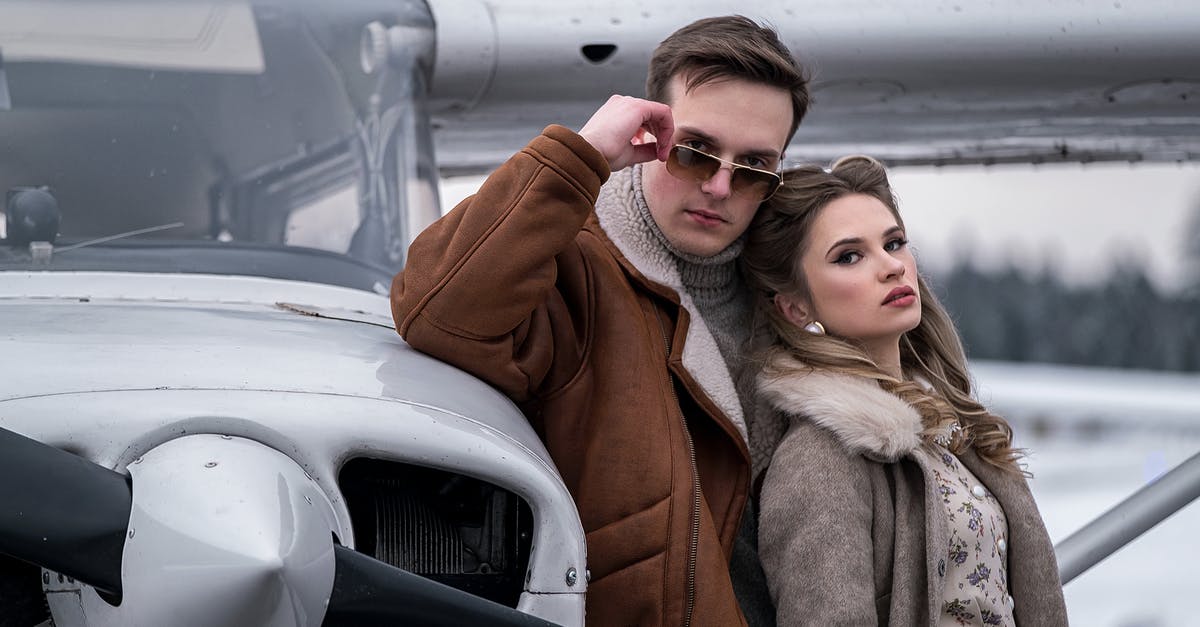 Cameras to the Delhi airport [closed] - Young couple in trendy warm wear standing close near turboprop airplane on winter airfield and looking at camera