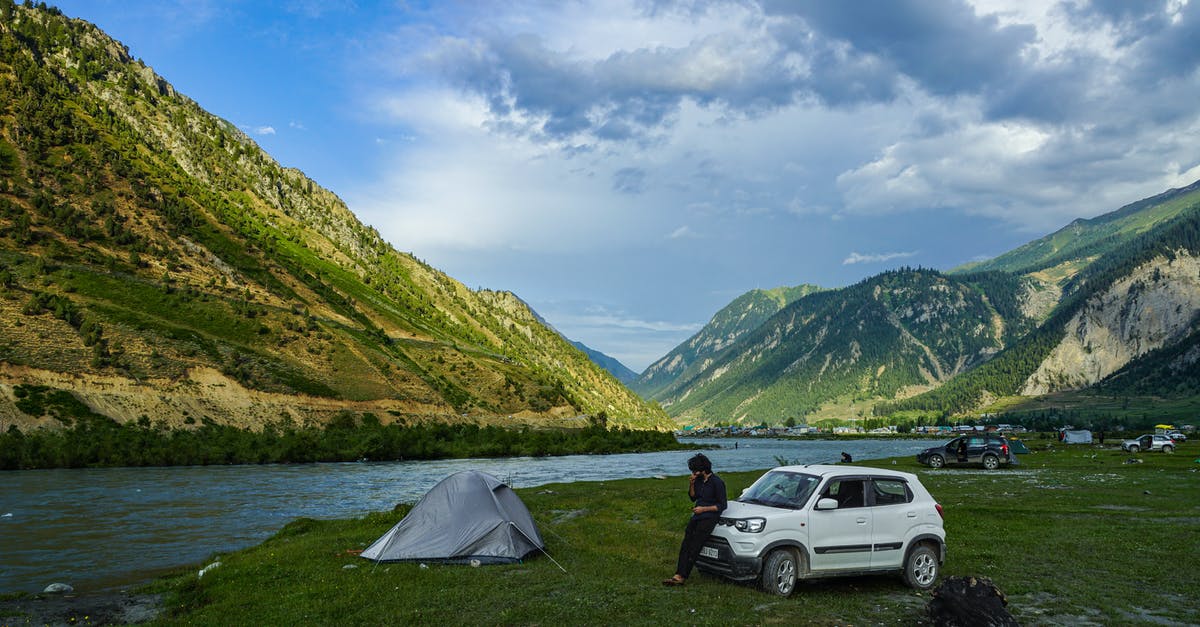 Camping facilities in Yellowstone and Grand Teton in July - Man in Black Shirt Sitting on Ground Beside White Suv