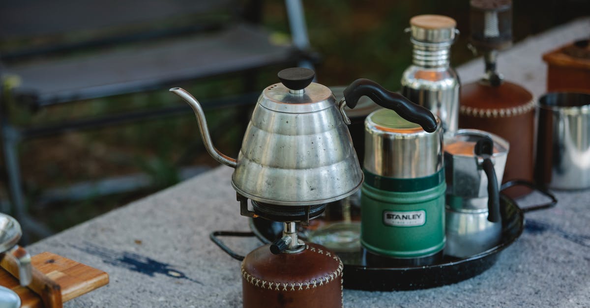 Camping stove on a plane? - High angle of metal coffee kettle placed on small portable camping gas stove near various utensils on table in nature