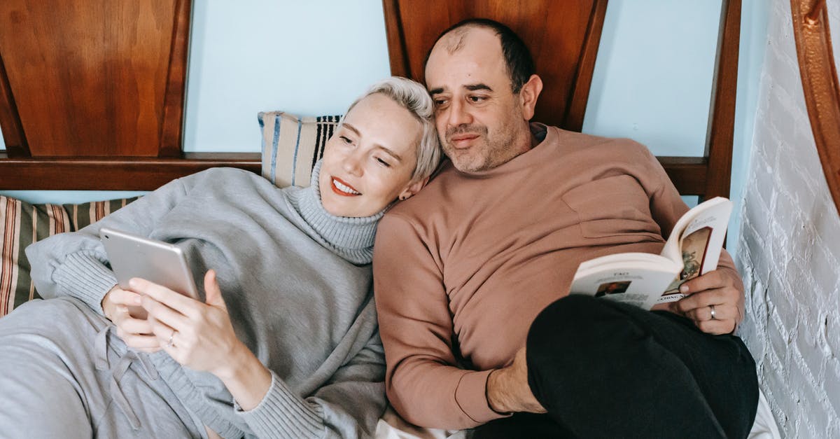 Can't book company reserved seats for spouse [closed] - High angle of happy adult woman using tablet and cuddling with ethnic husband reading interesting book on bed at home