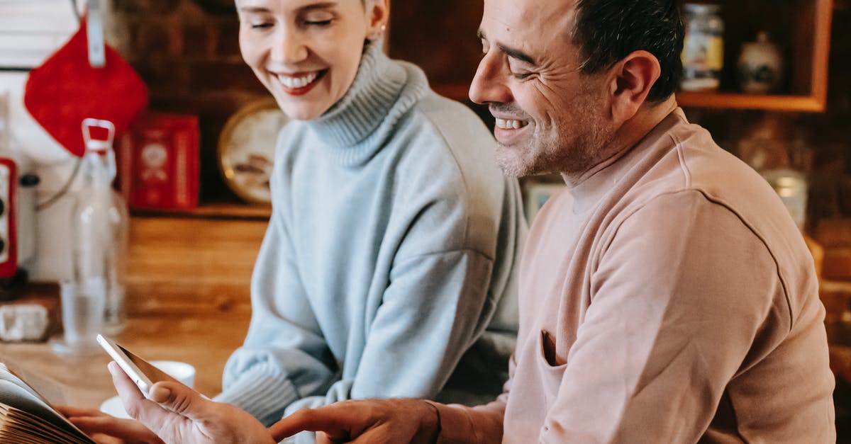 Can't book company reserved seats for spouse [closed] - Side view of crop positive multiracial spouses in casual clothes smiling while watching video on tablet sitting at wooden table in kitchen