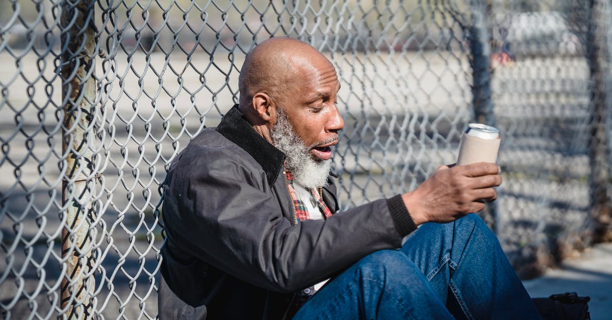 Can a 16 year old fly alone in the European Union? - Side view of black homeless bald man sitting on street with beer can in hand and leaning on wire railing