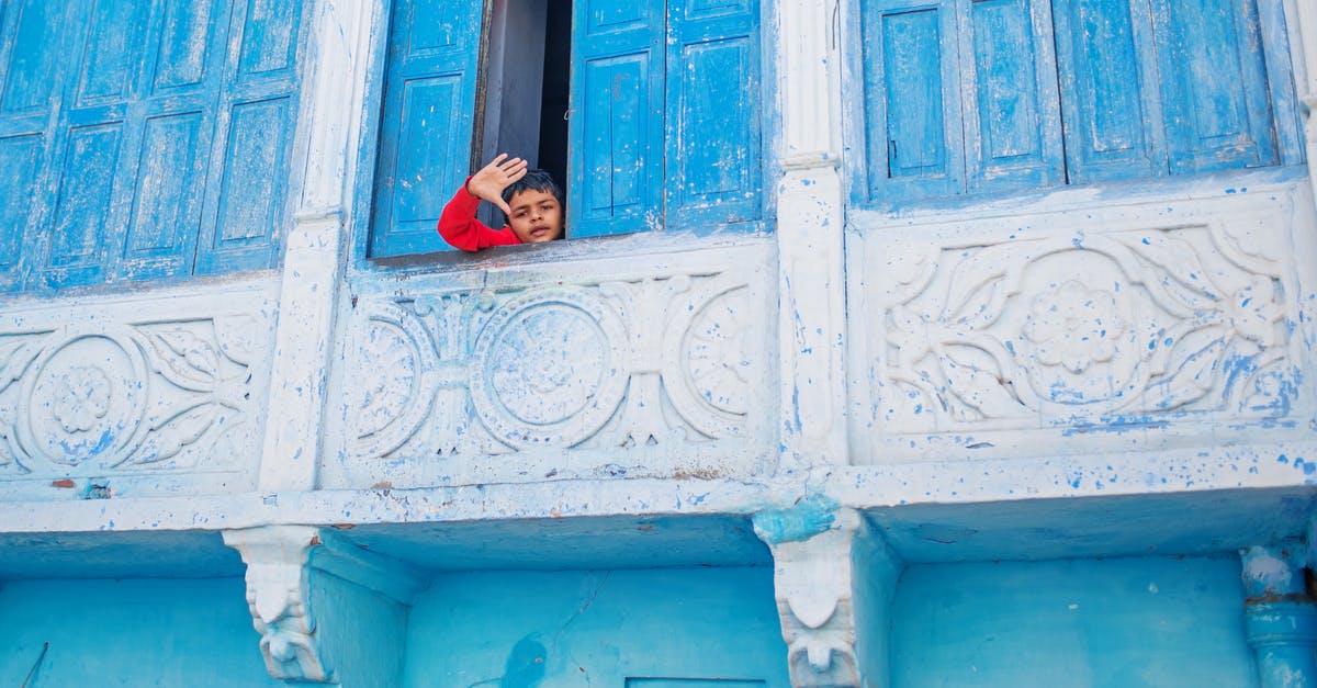 Can a child enter the UK on an accompanied visa and then leave the country alone? - From below of little ethnic boy waving at camera standing behind shabby shutters of blue balcony