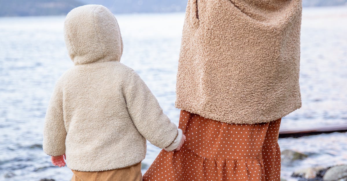 Can a child with accompanied visa travel back to home country with mother - Anonymous baby holding skirt of crop woman near river in winter countryside Can a child with accompanied visa travel back to home country with mother - Anonymous baby holding skirt of crop woman near river in winter countryside