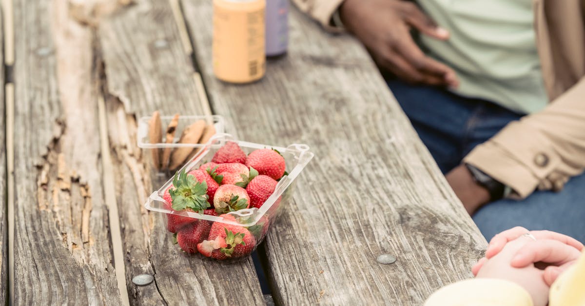 Can air rules change between booking time and date of travel? - Crop anonymous couple sitting at shabby wooden table with strawberries and cookies near cans of soda while spending time in park