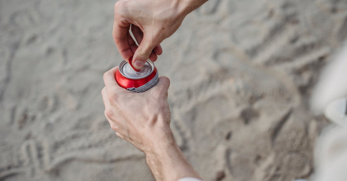 Can anyone identify this beach? - From above of crop anonymous male opening can of drink standing on sandy beach