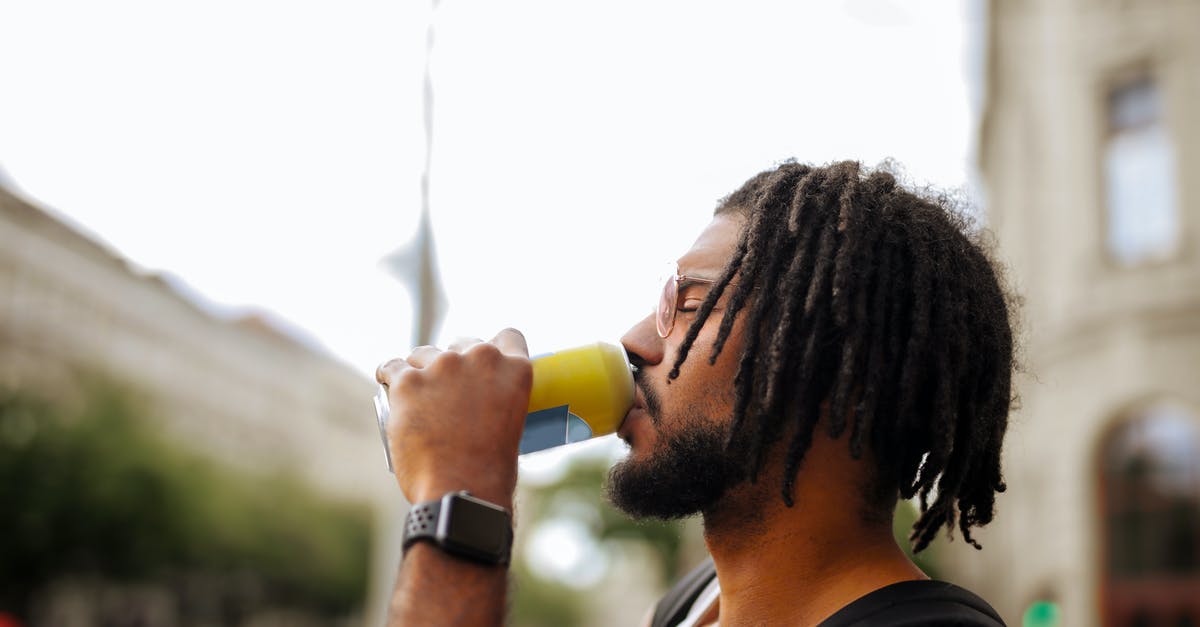 Can anyone identify this city skyline? [closed] - Side view of adult Hispanic guy with dreadlocks in sunglasses and casual clothes with backpack and smart watch drinking yummy beverage from vivid yellow can while standing with eyes closed on street in downtown