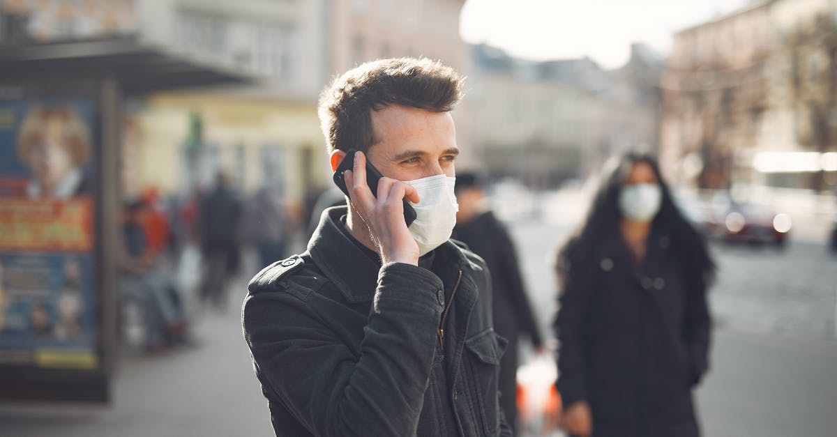 Can Apple World Travel Adapter Kit be used in Iran - Attentive male wearing warm jacket and protective facial mask standing not far from bus stop during phone call on city street in cold season