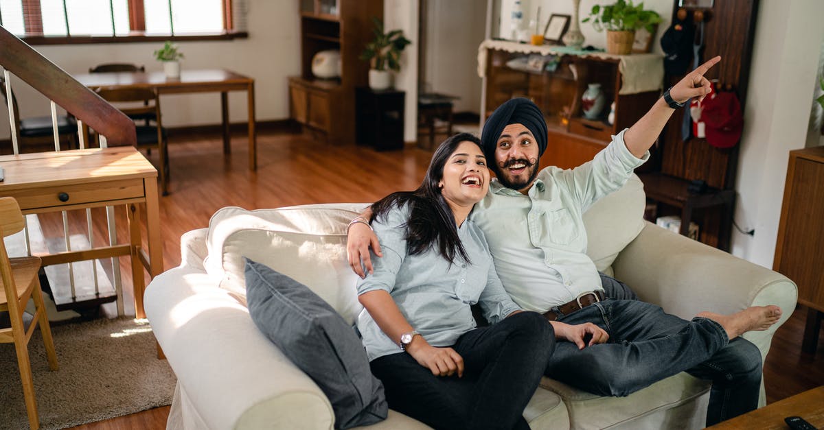 Can having a second wife affect my Australian visa processing/stay? - From above of smiling Indian man and woman in casual wear enjoying free time and chilling on sofa in modern light room while boyfriend pointing finger side up