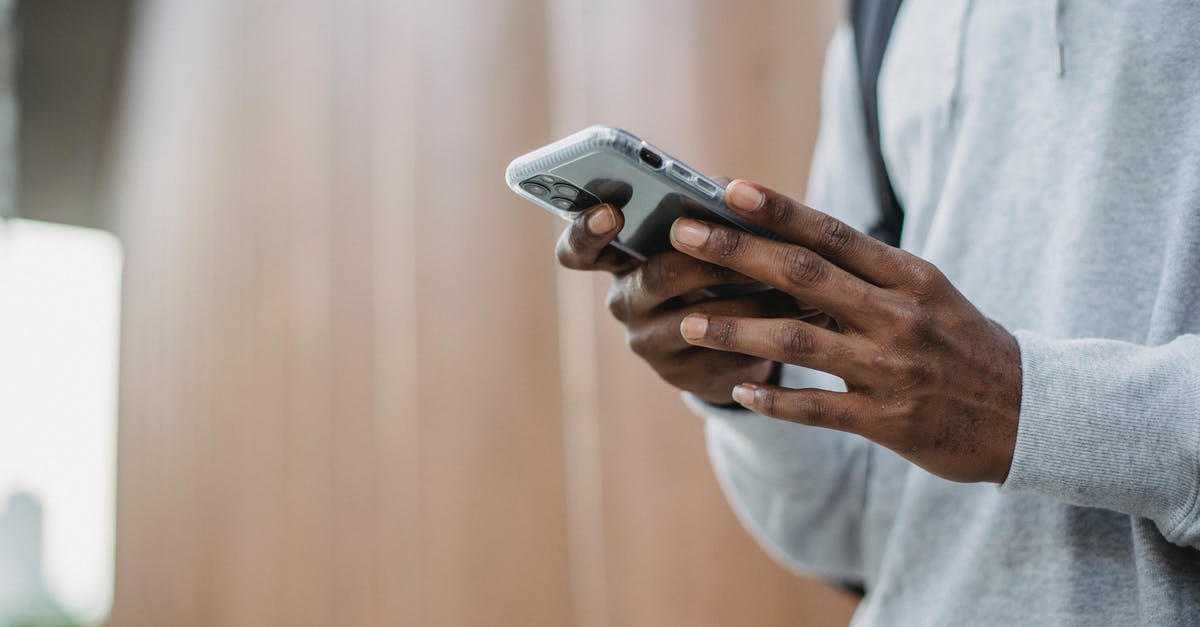 Can I add checked bags after online check-in (American) - From below crop of unrecognizable African American young guy in casual clothes messaging on mobile phone while standing near wooden wall