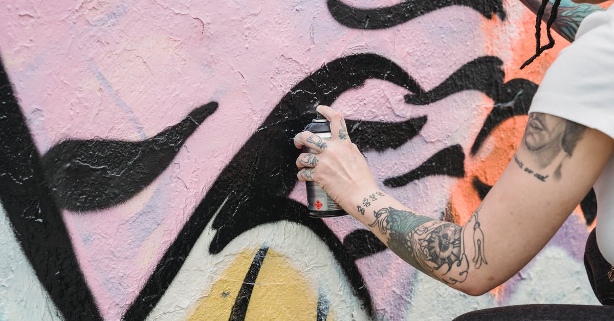 Can I apply for a Schengen visa from the UK if I am on a tier 5 temporary workers visa? - Side view of crop unrecognizable female artist with tattoos spraying paint on colorful wall with black patterns on street in city