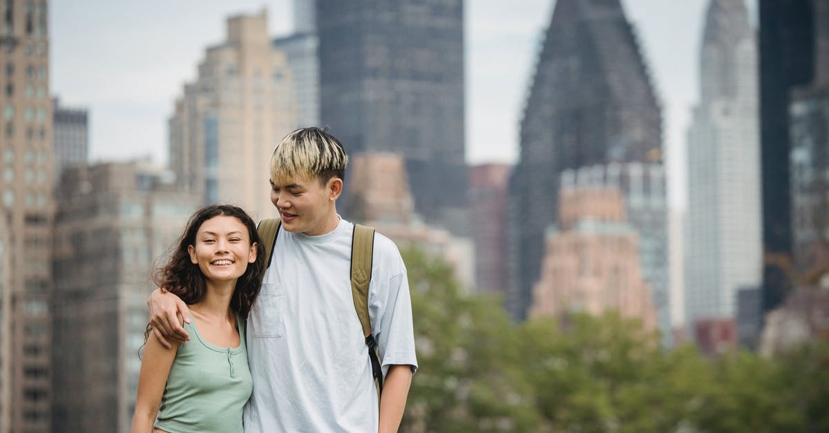 Can I apply for US driver's licence when visiting for a couple of months with J-1 visa? - Cheerful young Asian couple in casual clothes hugging each other and standing against modern skyscrapers while spending holidays in New York