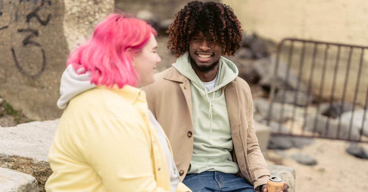 Can I ask for an earlier UK visa start date? - Cheerful multiracial couple with cans of soda sitting on stones on embankment near river while spending time together during date