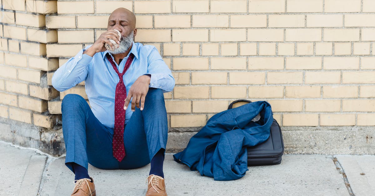 Can I avoid a full body scan going through security with a Nexus card? - Full body of mature African American bearded businessman in blue trousers and light shirt with maroon tie sitting on ground at brick wall and drinking beverage from tin can