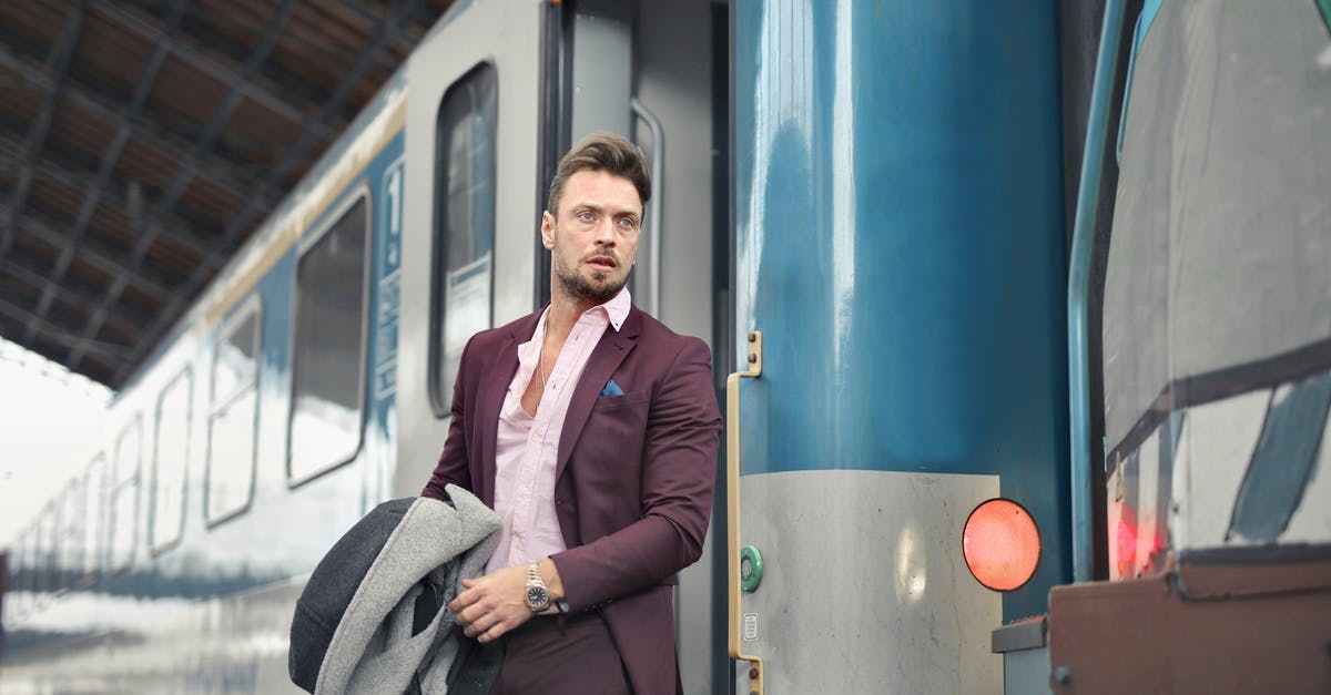 Can I bag wrap my suitcase at Leeds railway station? - Serious bearded male passenger in stylish suit standing near train with travel bag and coat in hand and looking away