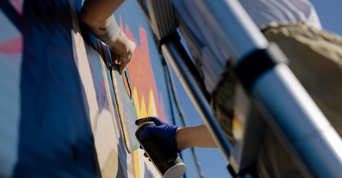 Can I bring a bear spray from the US to Canada? - From below of crop unrecognizable person in casual clothes and gloves using spray can while painting graffiti wall standing on ladder