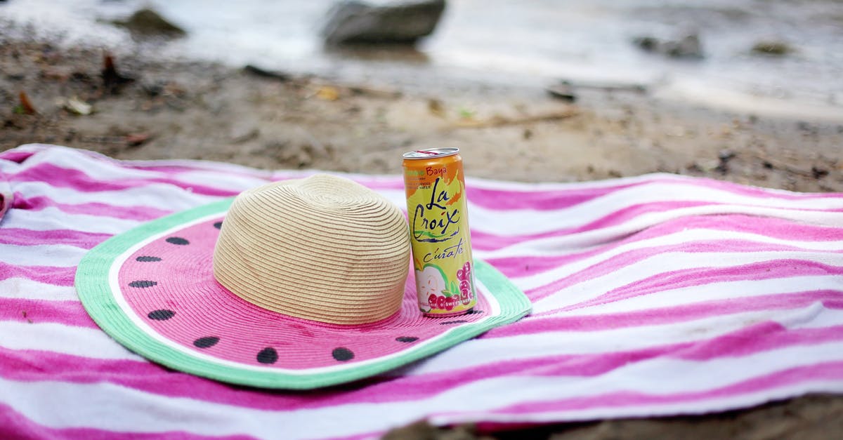 Can I bring a lightsaber from Disneyland into Australia? - Striped towel spread on sandy beach with straw hat and juice can