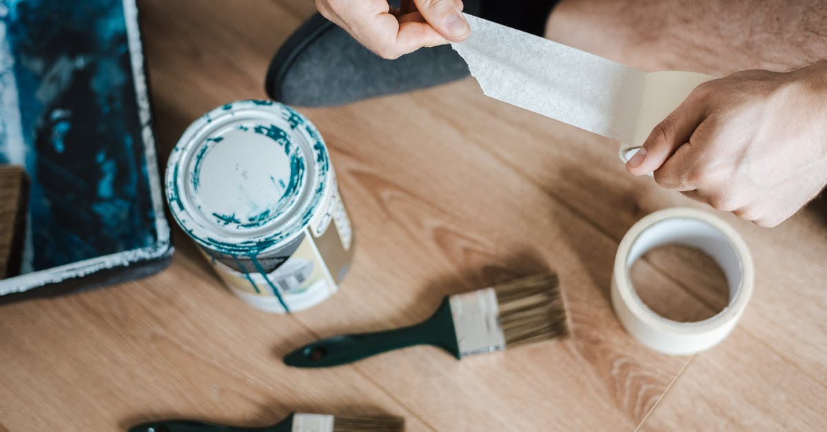 Can I bring a taser from Thailand to Sweden? - From above of crop anonymous male unwrapping sticky tape roll on parquet near paint brushes in house