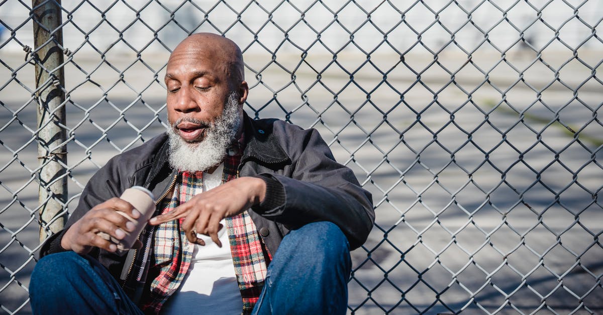 Can I bring an old artillery shell on a plane? - Hairless black male looking at beer can in hand against mesh fence in daylight