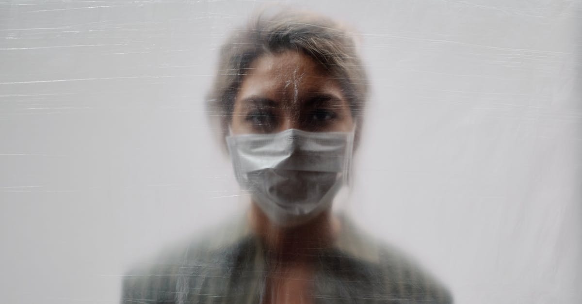 Can I bring gold sheet face masks in my carry on? - Woman in Striped Green Top and Face Mask Behind a Translucent Sheet