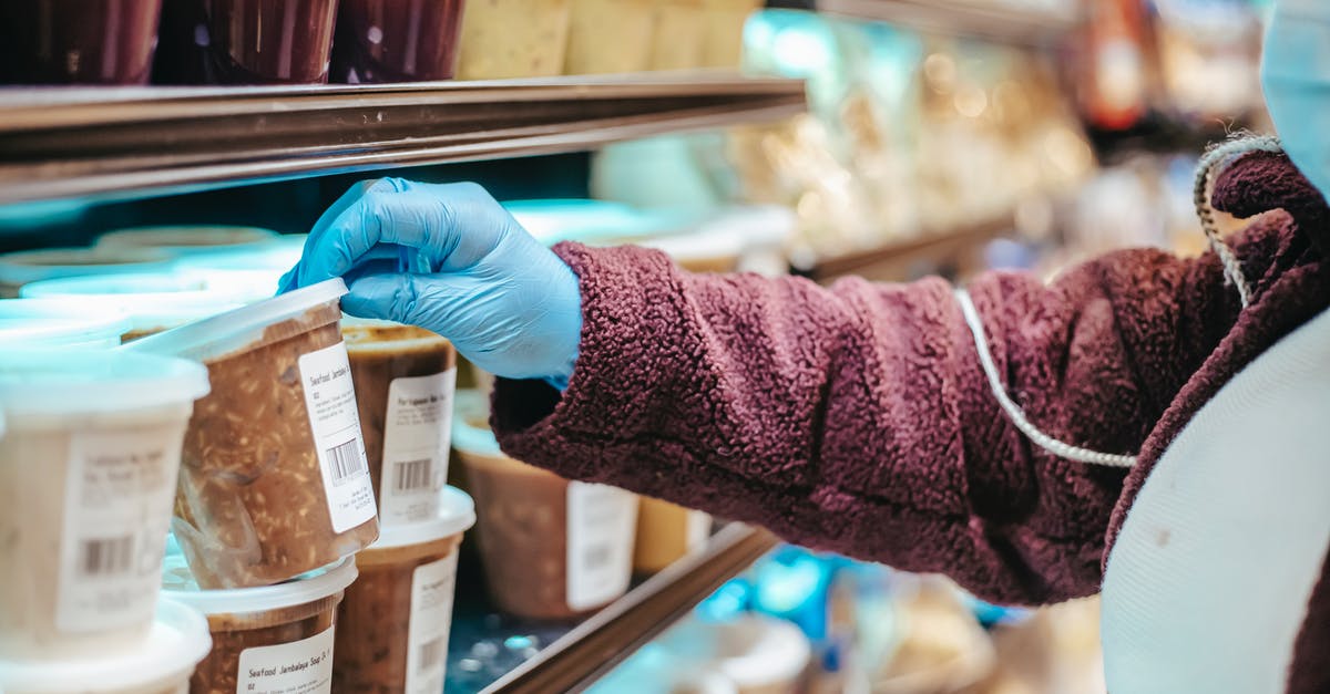 Can I buy a select seat at the check-in counter? - Crop anonymous female customer in protective mask reading label on frozen food in plastic container in grocery store