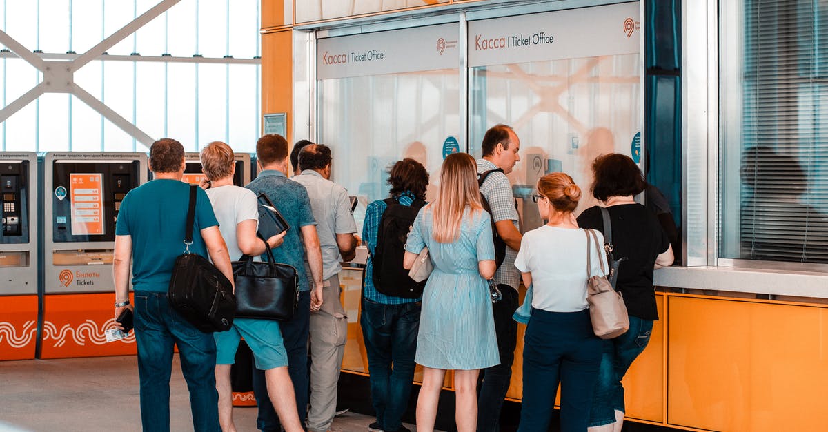 Can I buy two one way tickets for a trip? - Back view of unrecognizable people in casual wear standing near ticket office in public place