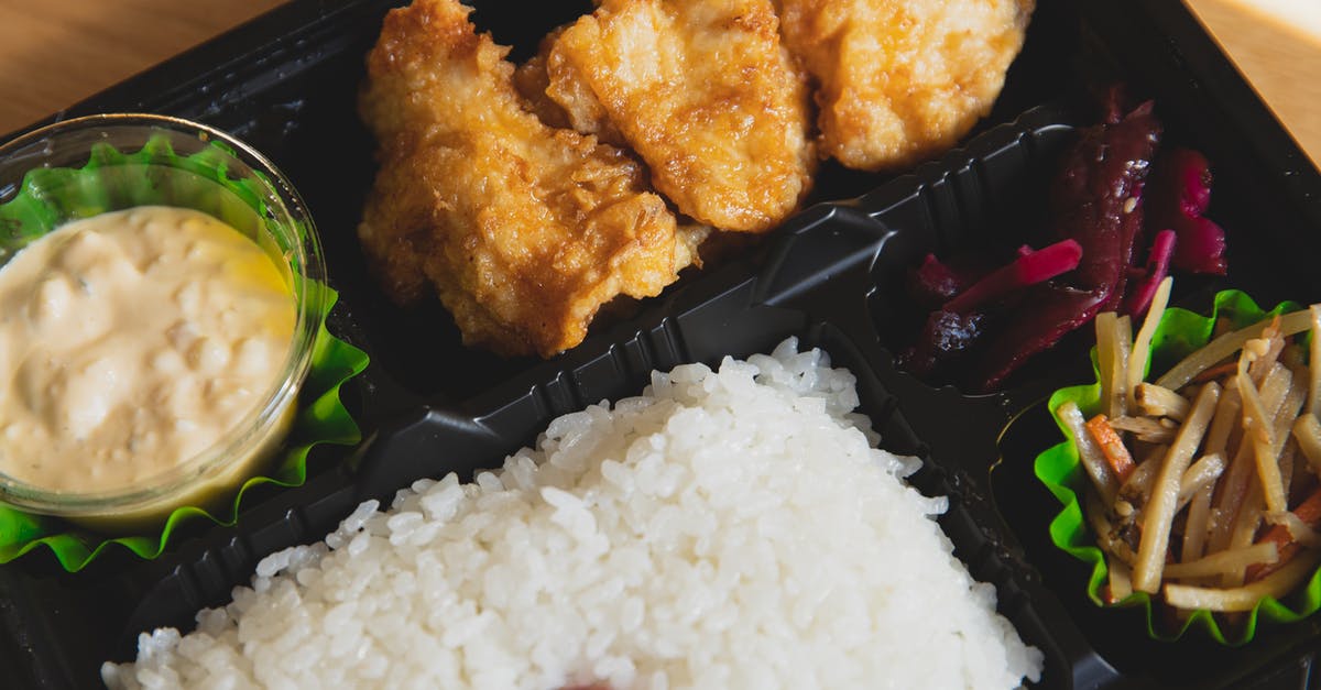 Can I carry fried rice and dried chicken preparation? - From above of plastic container with fried chicken and rice with sauce near sauce and sliced vegetables